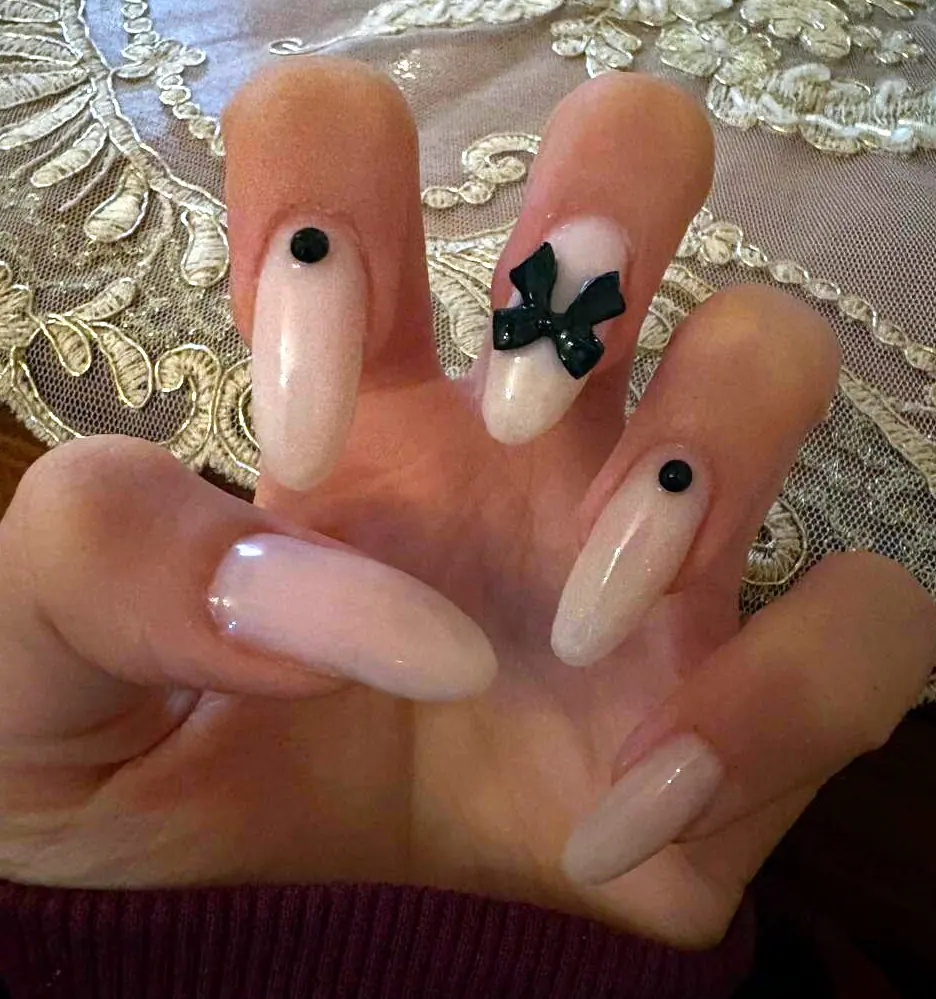 Long nude almond nails with glossy black 3D bow and stud accents